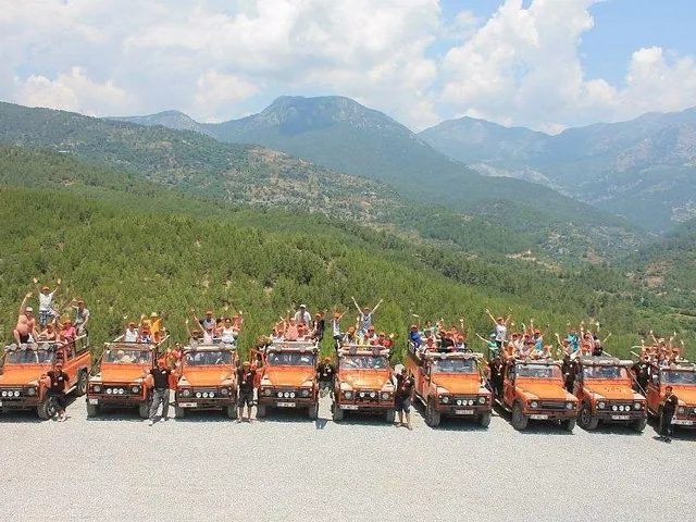 Eine große Gruppe von Menschen steht neben einer Reihe orangefarbener Open-Top-Jeeps.