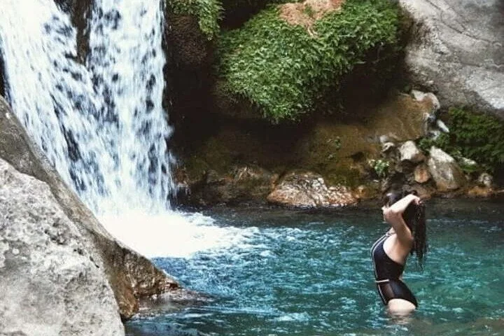 Eine Frau in einem schwarzen Badeanzug steht in einem Wasserbecken in der Nähe eines Wasserfalls.