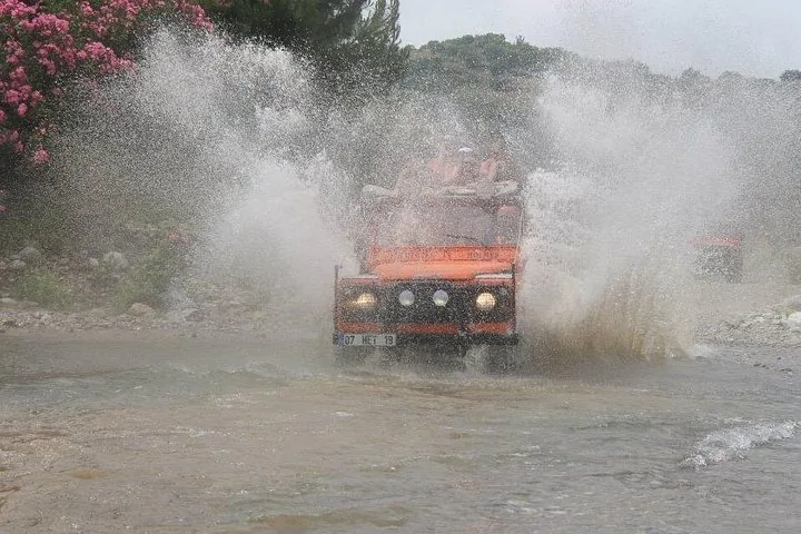 An orange open-top jeep splashing through a shallow river crossing.