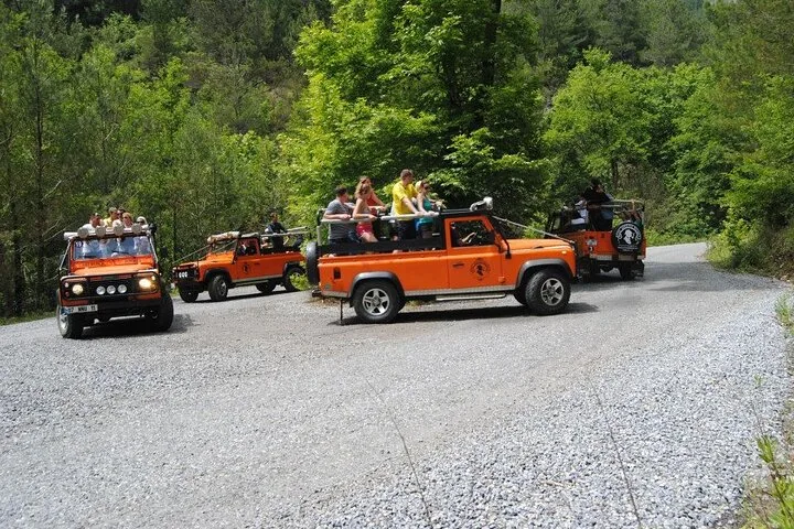 A group of orange open-top jeeps carrying passengers driving on a gravel road.