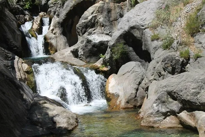 Water cascading down rocky steps in a small canyon surrounded by large boulders.