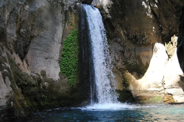 Ein gleichmäßiger Wasserstrahl, der in ein dunkelblaues Becken fällt, das von steilen Felswänden gesäumt ist.