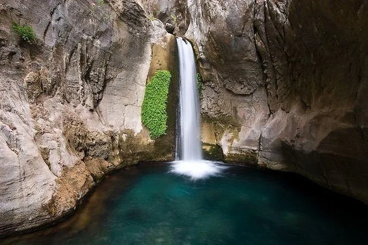 Ein Wasserfall stürzt in ein tiefes türkisfarbenes Becken, umgeben von steilen Felsklippen.