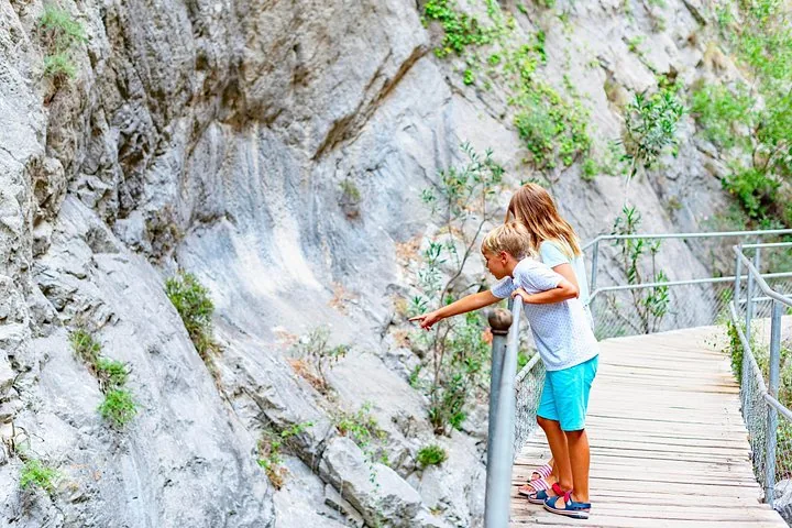 Zwei Kinder stehen auf einem Holzsteg und zeigen auf etwas an der felsigen Canyonwand.