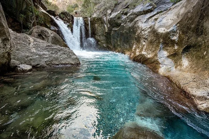 Klares türkisfarbenes Wasser fließt durch eine felsige Schlucht auf einen kleinen Wasserfall zu.