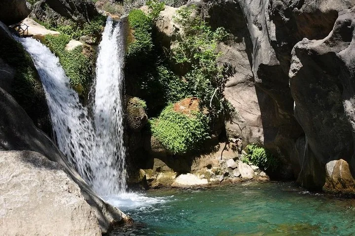 Ein Wasserfall stürzt über Felsen in ein klares, türkisfarbenes Becken in felsiger Umgebung.